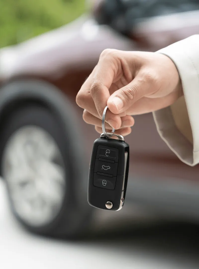 Hand holding a car key in front of a car