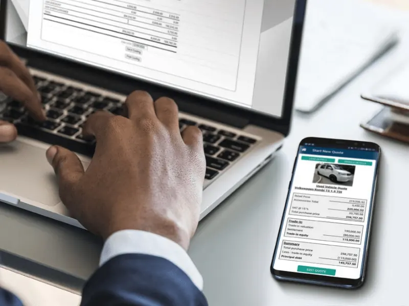 Salesperson typing on a laptop next to a phone showing an EasyQuote vehicle quote